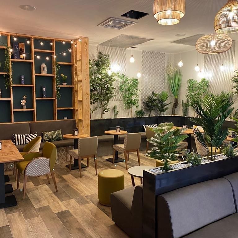 La sala illuminata: lampade in rattan, scaffalature in legno con lucine, poltroncine ocra e in tessuto chevron, divani grigi e piante.